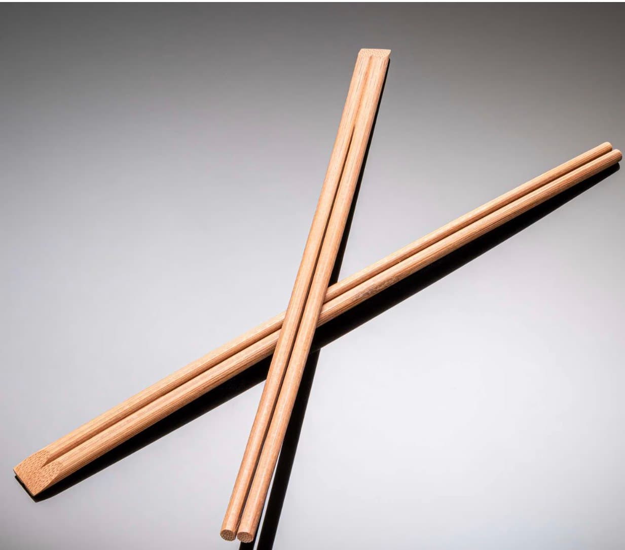 Close-up of natural bamboo Tensoge chopsticks crossed against a gray background